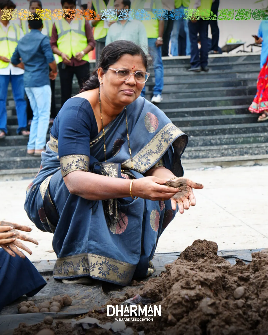 A teacher joining students on the ground to roll seed balls.