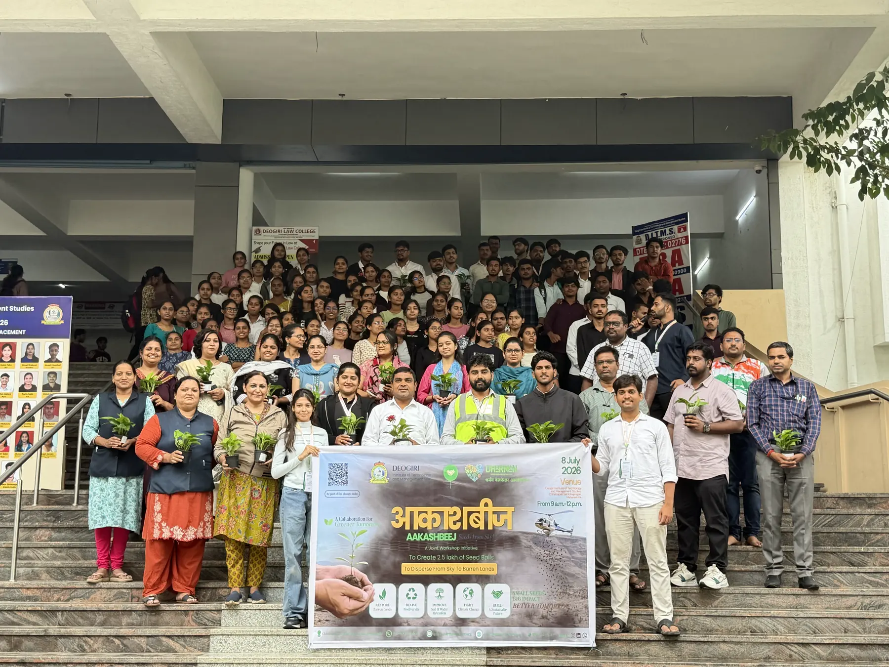More than a hundred volunteers and students on the steps at Deogiri College, each holding a sapling, behind the Aakashbeej seed-ball workshop banner.